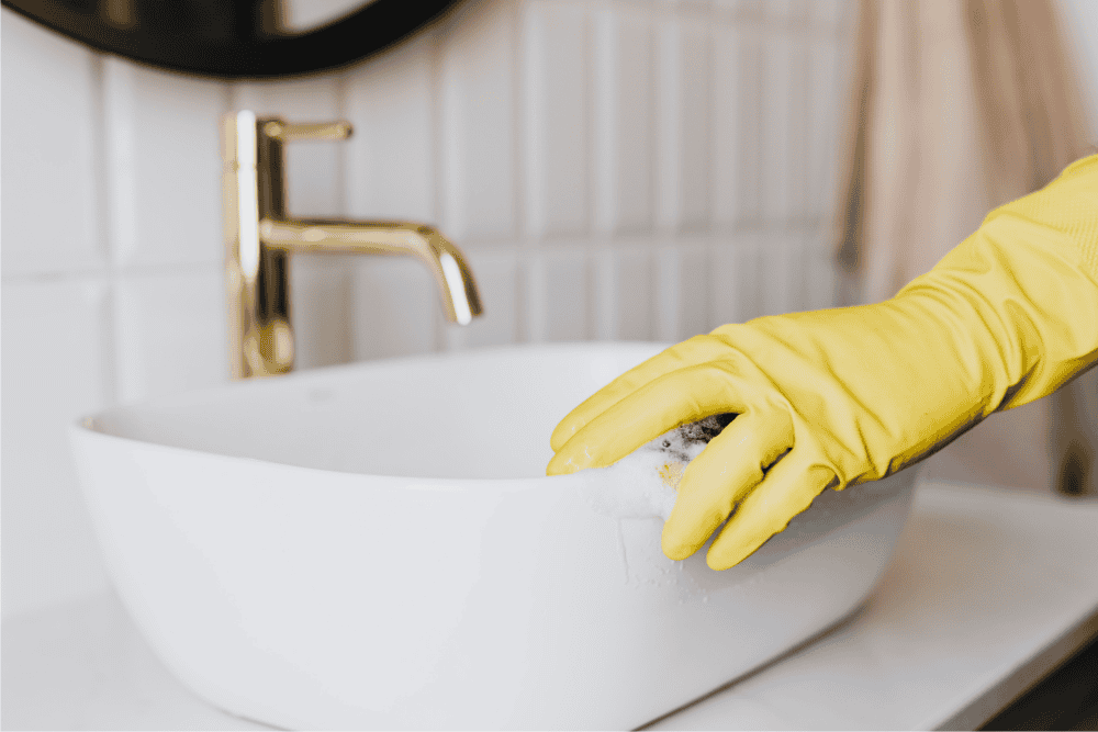 Professional cleaner scrubbing bathroom sink and sanitizing toilet during bathroom cleaning service