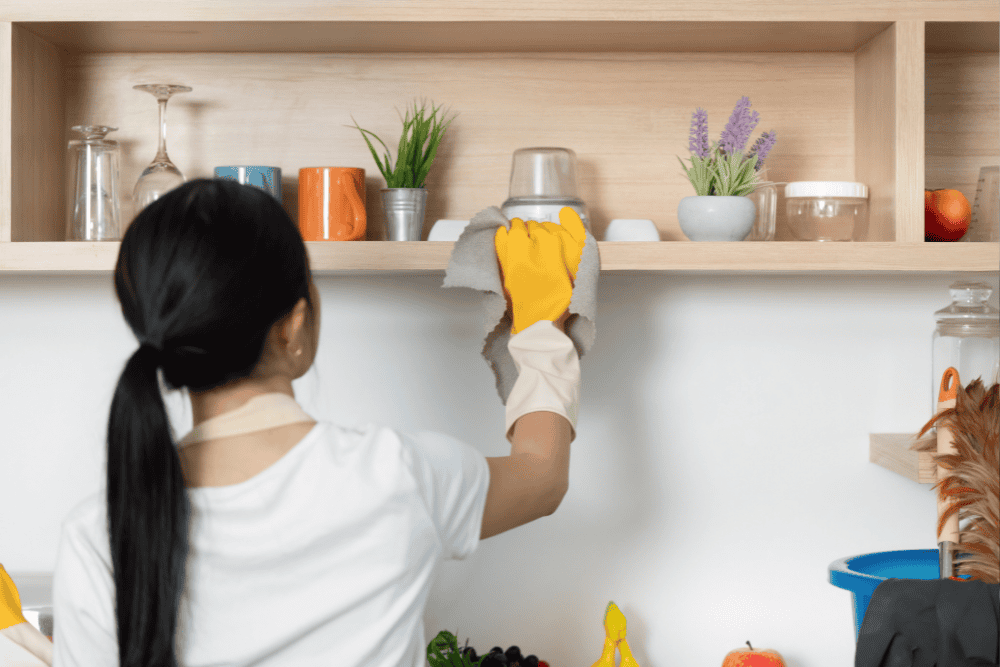 Professional maid dusting shelves and electronics with microfiber cloth during home cleaning