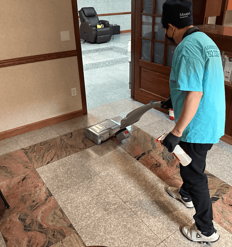 Technician deep-cleaning medical office stone tile flooring using a professional-grade autoscrubber for a hygienic, polished finish.